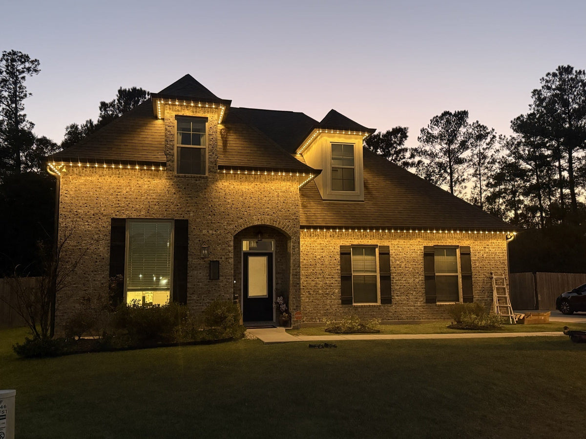 A real ShowHome installation: warm-white lights outlining a brick home and its dormers at dusk