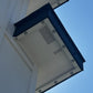 An upward-looking view of a white exterior wall corner with dark blue trim and multiple recessed light fixtures, set against a clear blue sky.